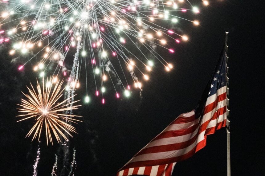 Fourth of July fireworks light up the night sky above an American flag