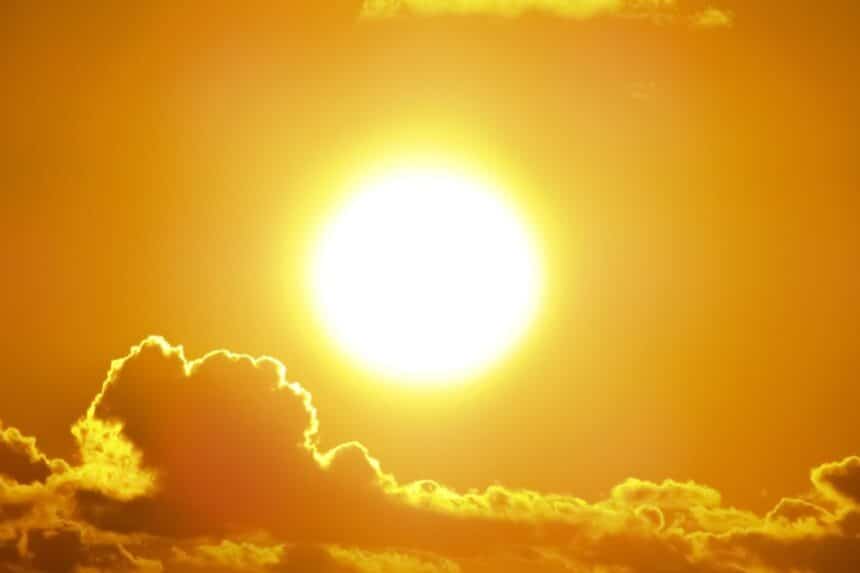 A blazing summer sun in a golden sky above dark clouds
