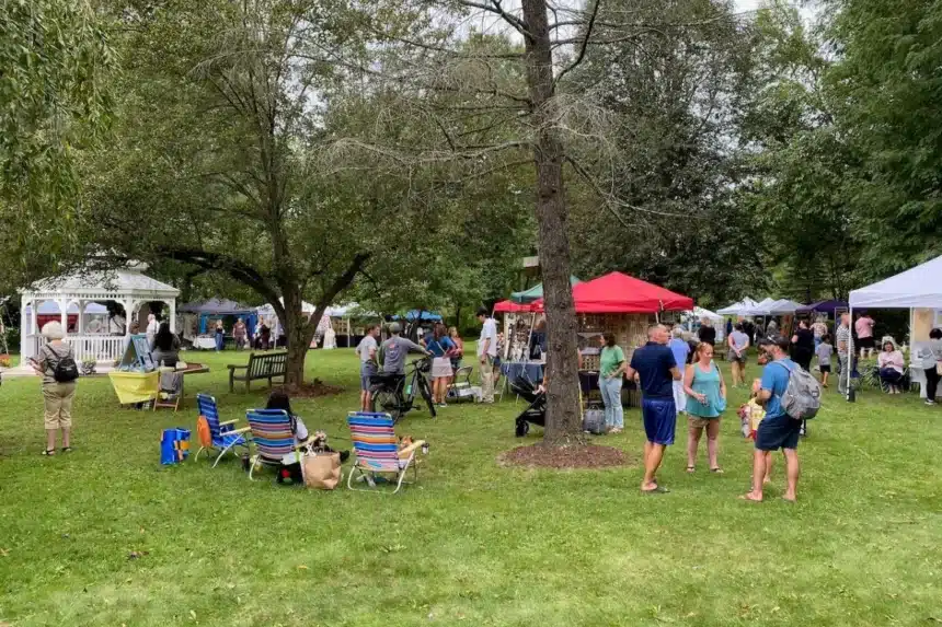 Visitors walk among white and red vendor tents under shade trees on the lawn at Hogan’s Memorial Park during the Denville Arts Council Art in the Park show.
