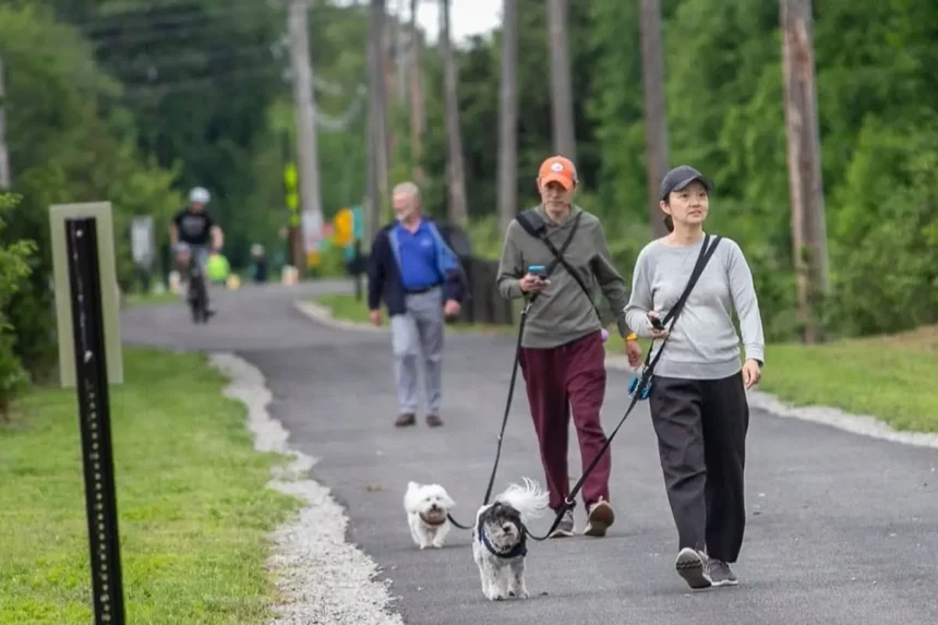 Walkers with dogs and a cyclist share a paved rail trail lined with trees in North Jersey