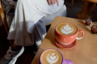 Two lattes with latte art on a sunlit wooden cafe table