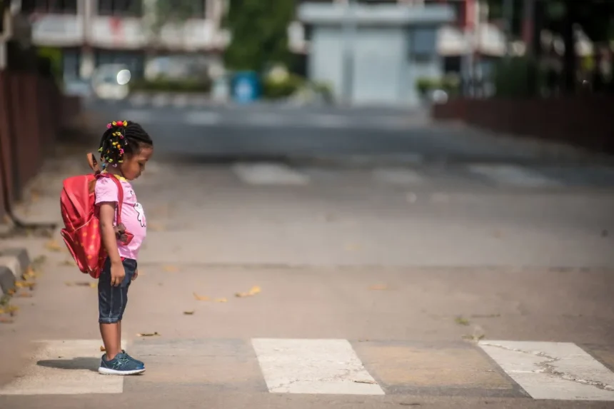 Child with a backpack waiting at a crosswalk, illustrating Safe Routes to School sidewalk projects