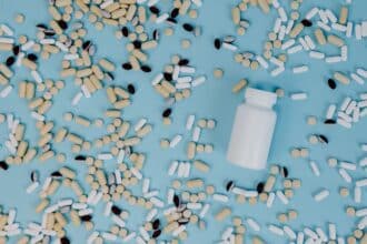 Assorted pills and capsules scattered around a white medicine bottle on a blue background.