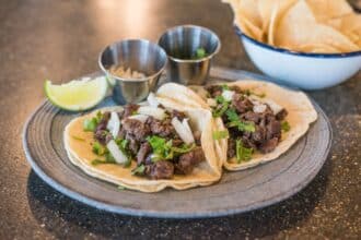 Beef tacos topped with onion and cilantro with a lime wedge