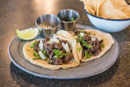Beef tacos topped with onion and cilantro with a lime wedge