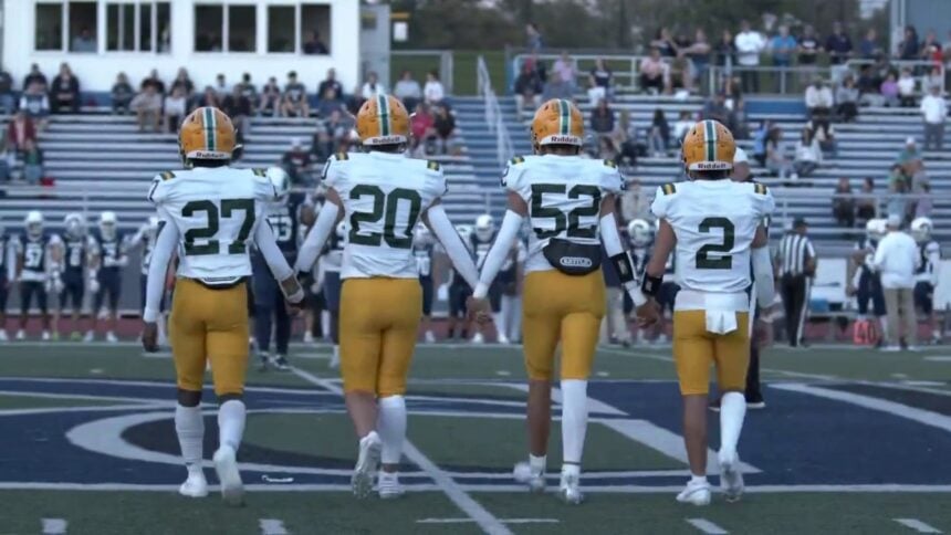 Morris Knolls Golden Eagles football captains in gold helmets and white jerseys walk to midfield for the coin toss
