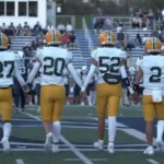 Morris Knolls Golden Eagles football captains in gold helmets walk to midfield for the coin toss