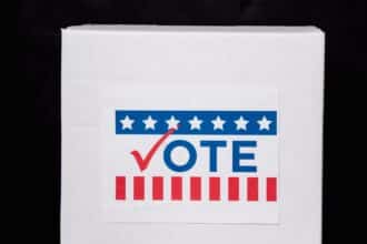 White ballot box with a VOTE sign and voting stickers on a table